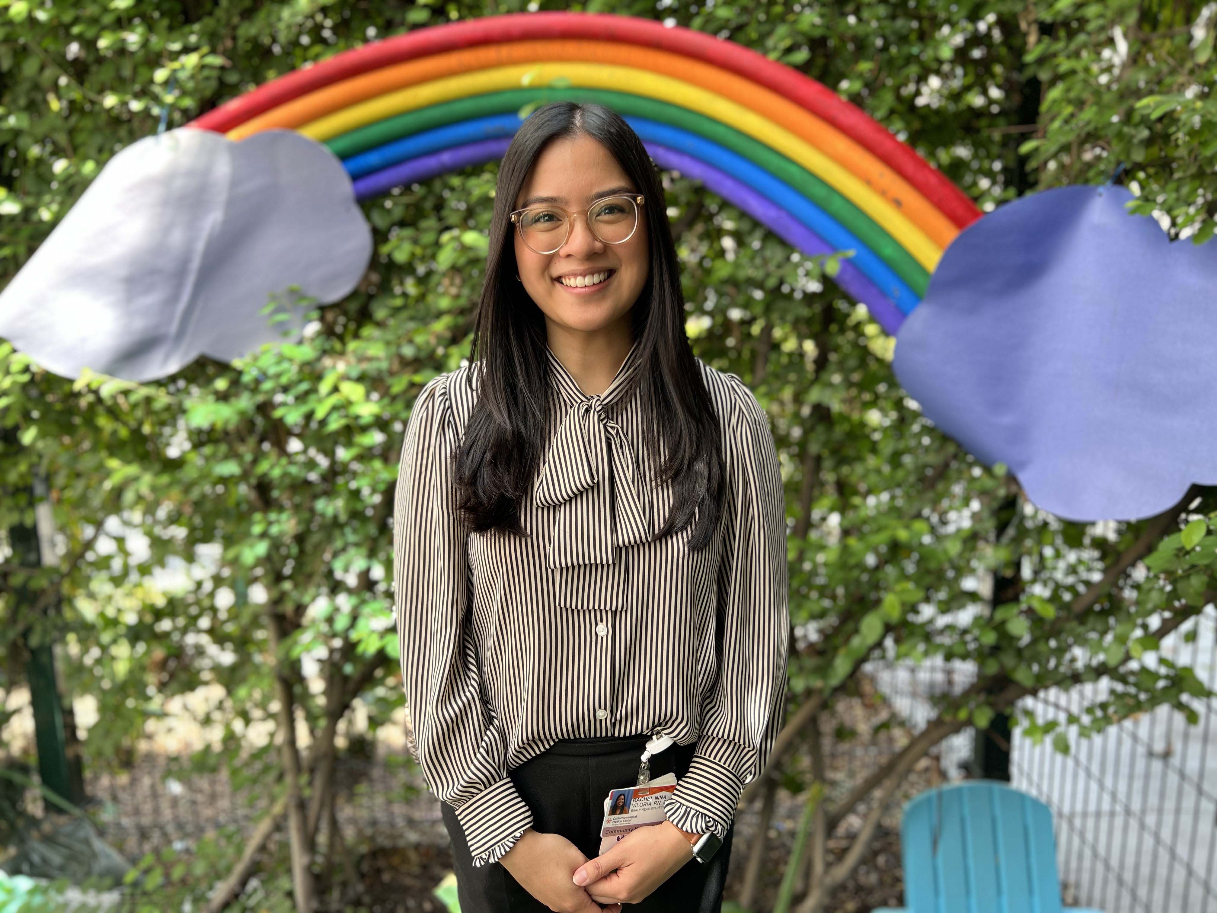 Hope Street Margolis Family Center Health Manager Rachel Viloria smiling while standing in front of a handcrafted rainbow 